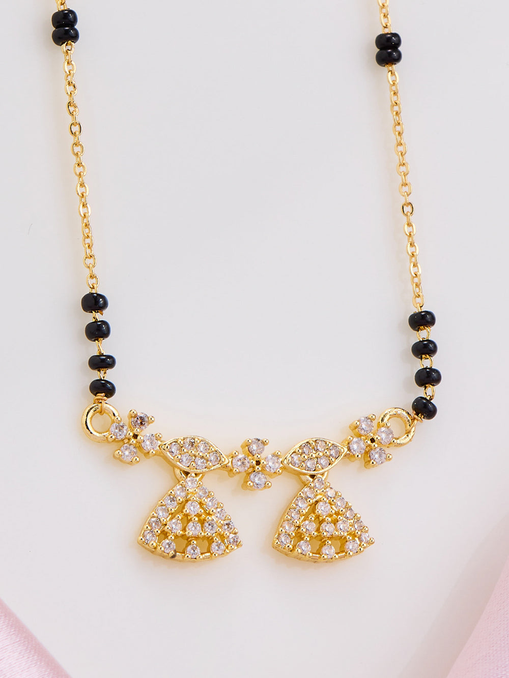Gold necklace with black beads on a light pink background
