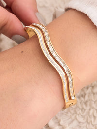 Gold bracelet with diamond accents on a wrist against a neutral background