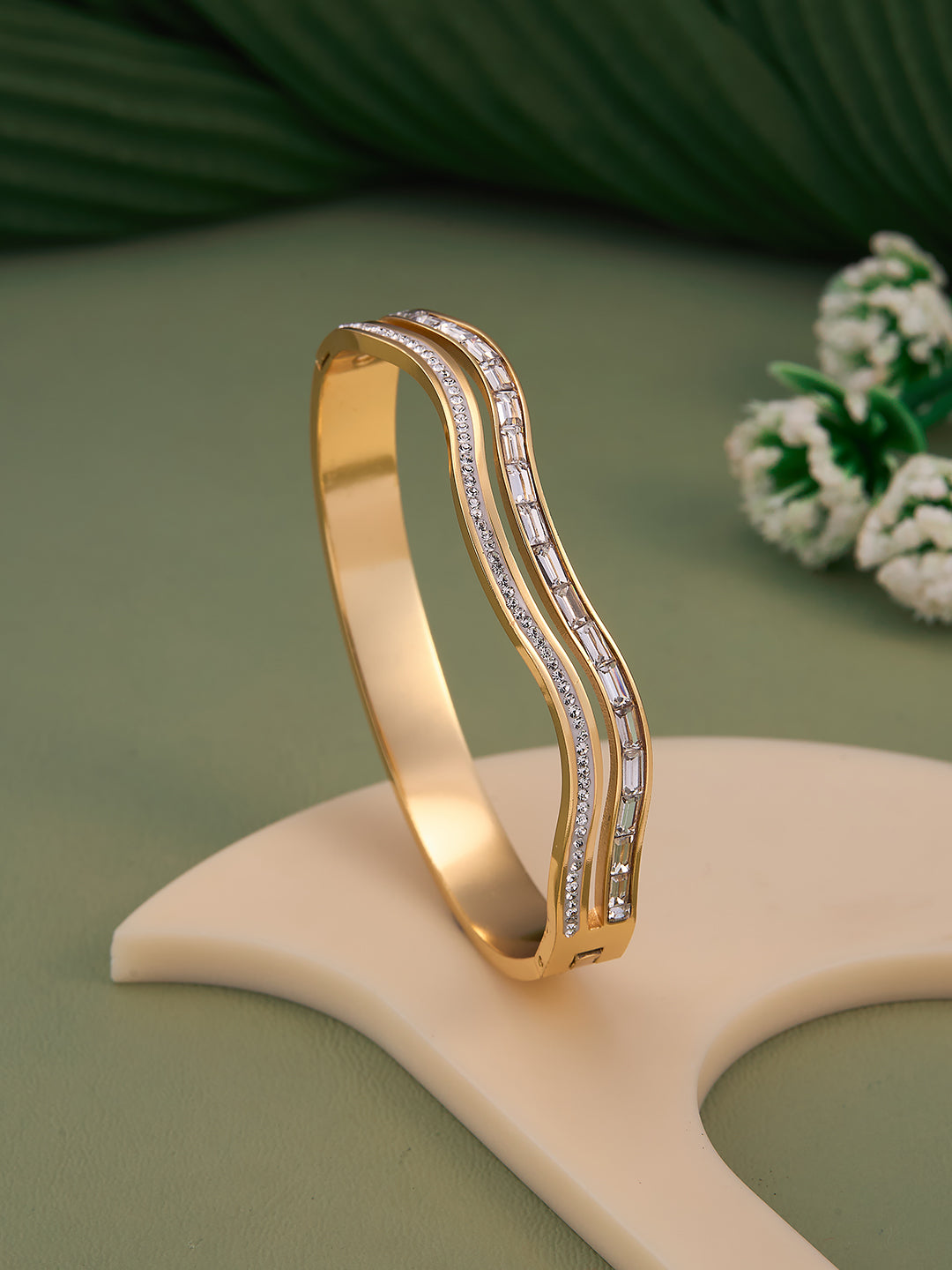 Gold bracelet with diamond accents on a beige stand against a green background