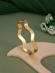 Gold bracelet with wavy design on a green background